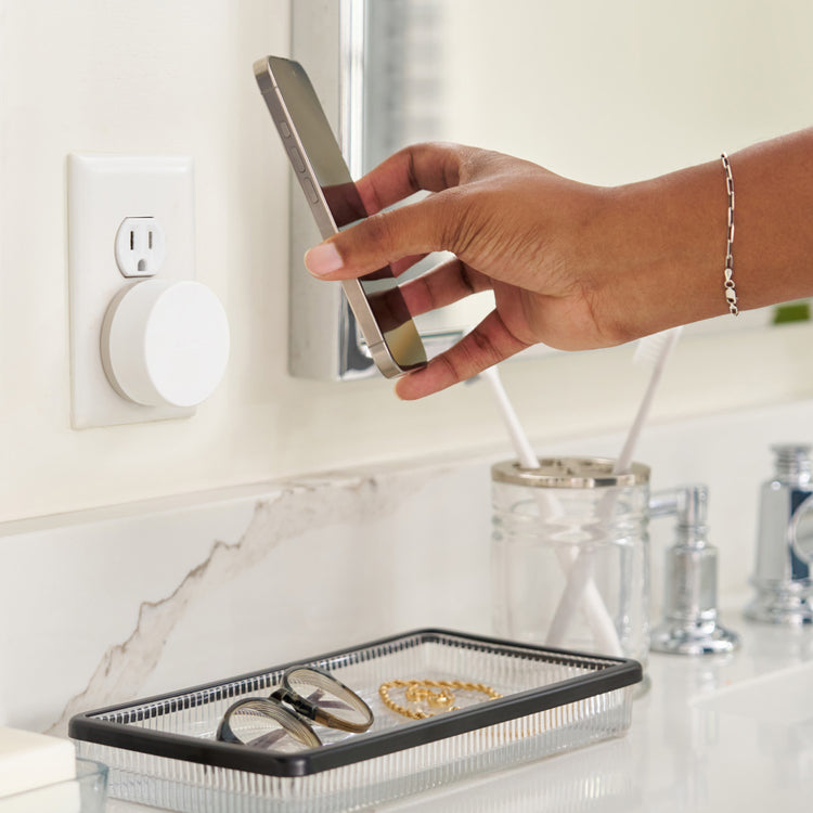 Person using a smartphone to control a smart light bulb on a bathroom counter.