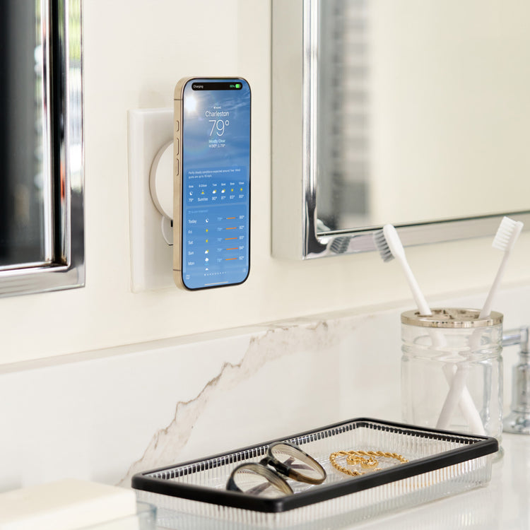 Smartphone mounted on a wall next to a mirror with a tray below containing jewelry and a jar with toothbrushes.