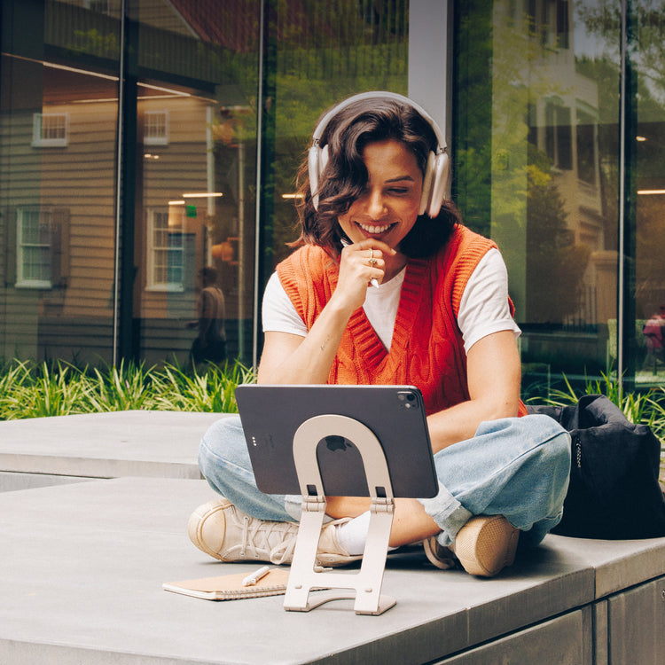 Woman sitting outdoors with headphones on, using a tablet.