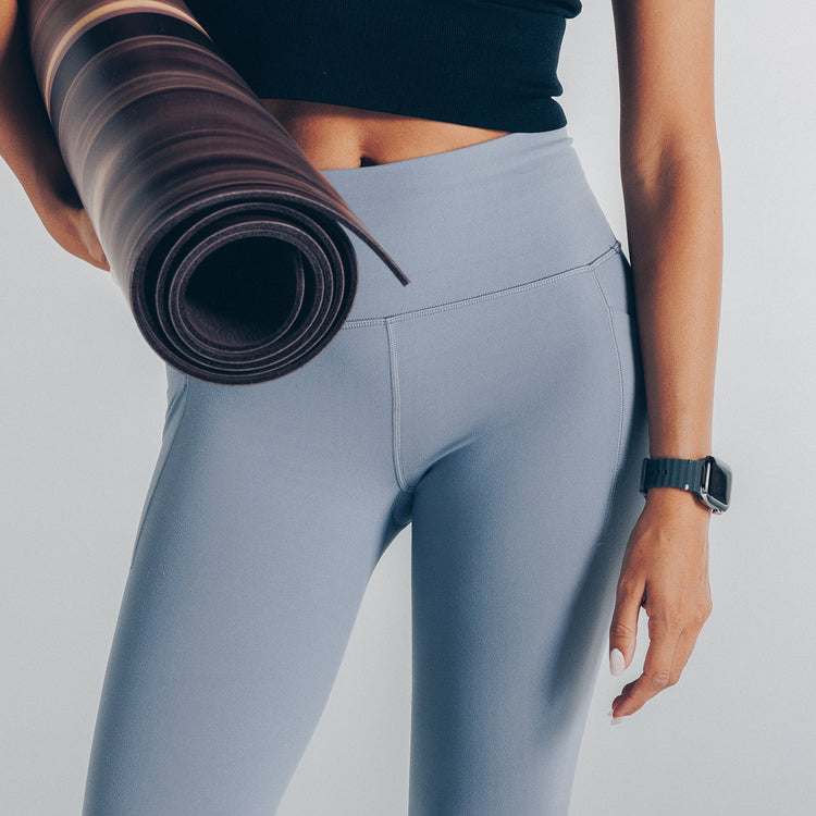 Person wearing gray leggings holding a yoga mat on a plain background