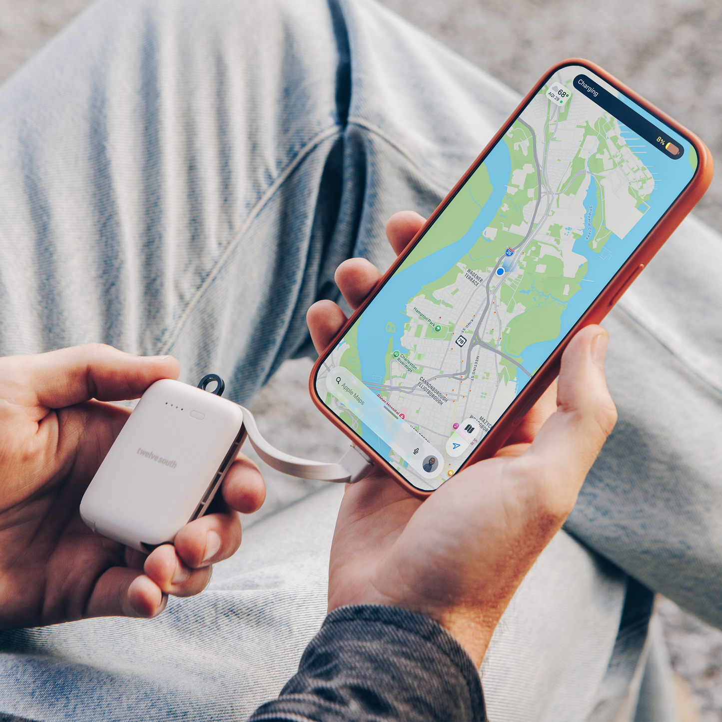Person holding a phone with a map app and a white device, possibly a power bank, in their other hand.