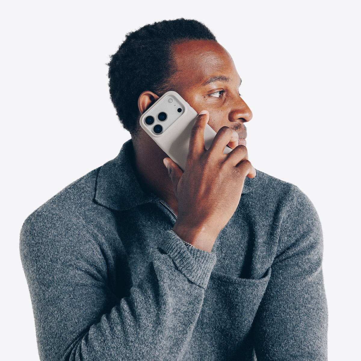 Man in gray sweater talking on a dune smartphone against a white background