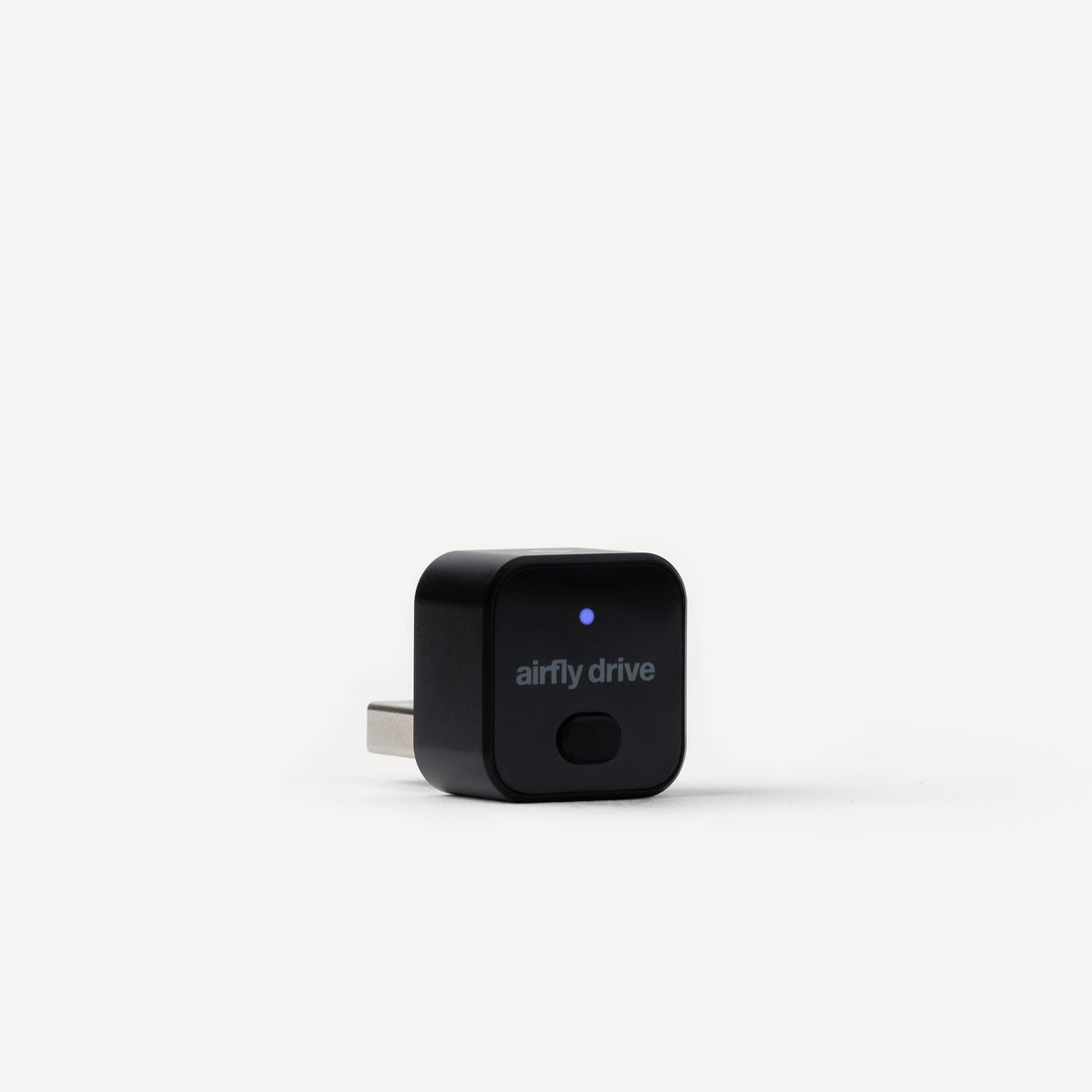 A black Airfly Drive plug-in device with a USB-C connector, featuring a small blue LED indicator light and the 'airfly drive' logo on the front, set against a clean white background.