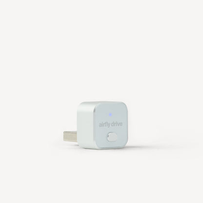 A small white square electronic plug with a USB-C connector, featuring the 'airfly drive' logo and a tiny blue indicator light, set against a clean white background.