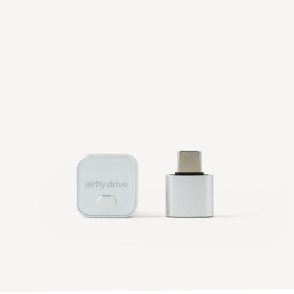 A small Airfly Drive USB-C adapter shown in two views on a clean white background: one view shows the square white branded case with the Airfly Drive logo, and the other shows the USB-C connector exposed.
